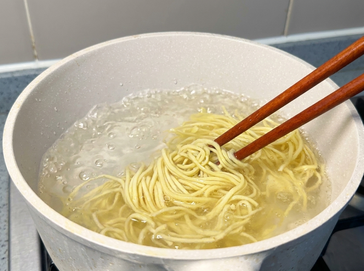 Frische gelbe Ramen-Nudeln werden mit Stäbchen aus einem Topf mit sprudelnd kochendem Wasser gehoben.