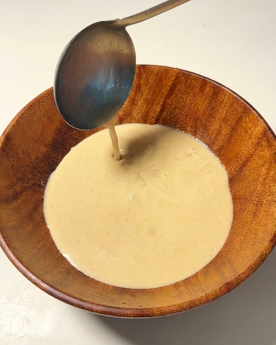 Heiße Schweinebrühe wird mit einer Schöpfkelle in eine Holzschale gegossen.