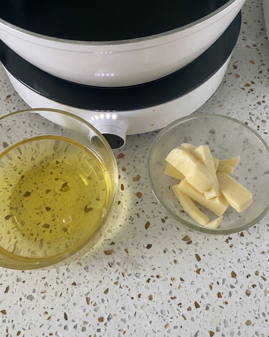 Zwei kleine Glasschüsseln mit aufgeschlagenen Eiern und Mozzarella-Scheiben auf einer weißen Arbeitsfläche neben einer Kochplatte.