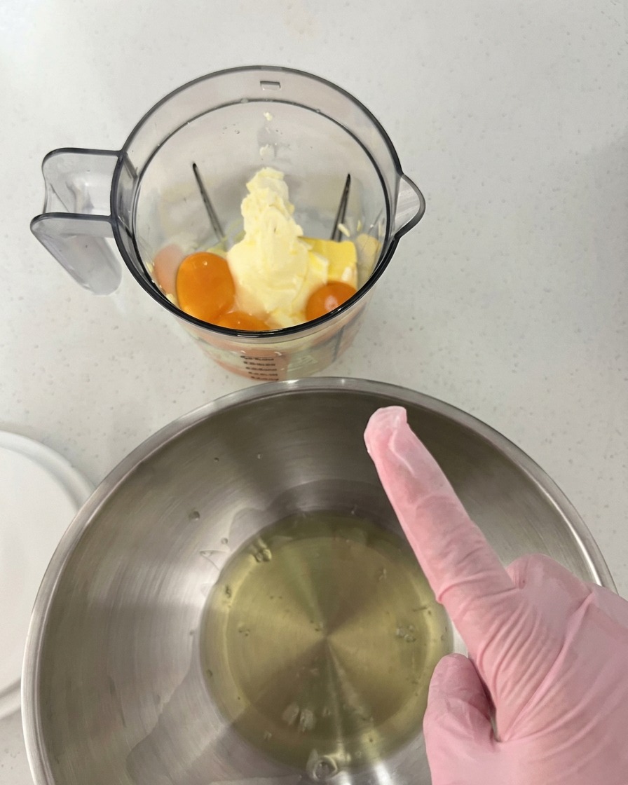 Eigelbe mit Butter und Frischkäse in einem Mixerbecher neben einer Edelstahlschüssel mit klarem Eiweiß.