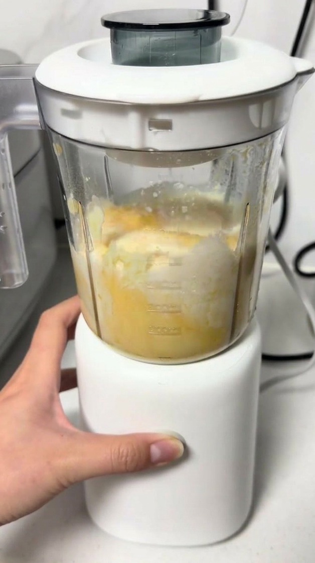 Ein Handmixer vermengt eine gelbe Käse-Ei-Masse in einem transparenten Becher.