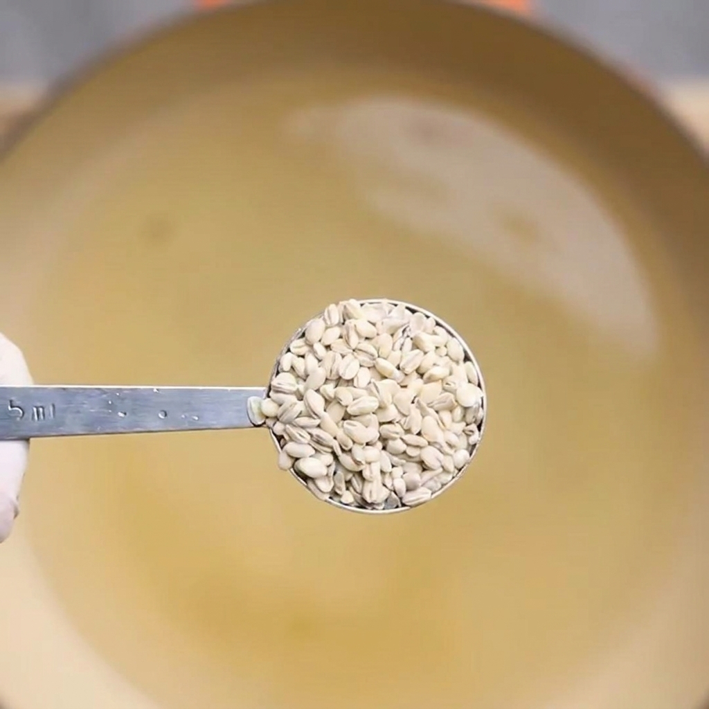 Gekochte Gerstenkörner werden mit einem Löffel aus dem Wasser gehoben.