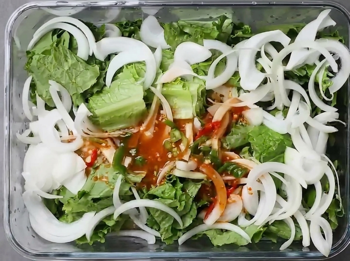 Roter Kimchi-Sud wird über den Salat und die Zwiebeln in einen Vorratsbehälter gegossen.