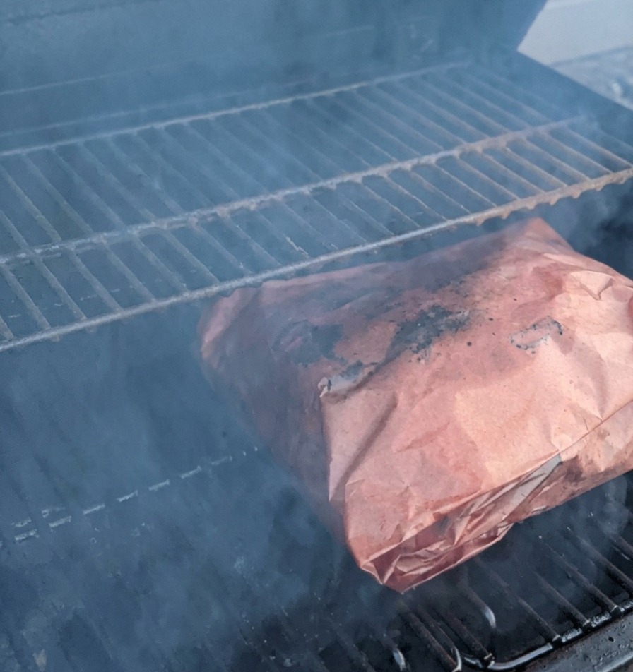 In Metzgerpapier eingewickelte Rinderrippen garen auf dem Smoker-Rost im dichten Rauch.