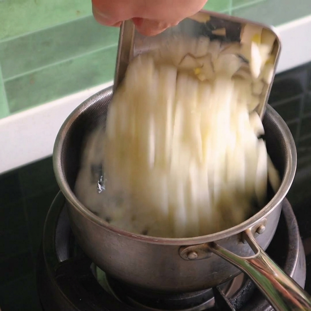 Gewürfelte weiße Zwiebeln werden von einem Schaber in einen kleinen Edelstahltopf auf einem Gasherd geschoben.