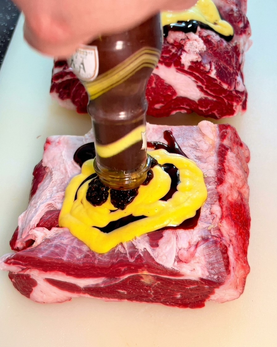 Dicke schwarze Pfeffersauce wird aus einer Glasflasche über die Senfschicht auf dem Rindfleisch gegossen.