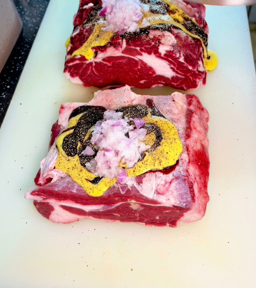 Rohes Rindfleisch, bedeckt mit Senf, dunkler Austernsauce und fein gehackten roten Zwiebeln auf einem Schneidebrett.