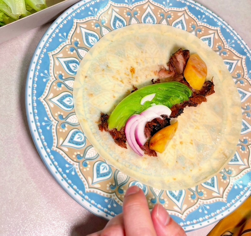Gehacktes geräuchertes Rindfleisch belegt mit Avocadoscheiben und roten Zwiebeln in der Mitte einer Tortilla auf einem dekorativen Teller.