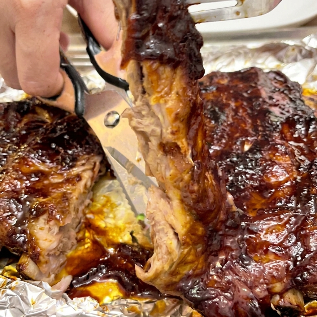 Nahaufnahme einer Küchenschere, die durch ein zartes, mit Sauce bedecktes Rippchen schneidet, um es vom Rack zu trennen.