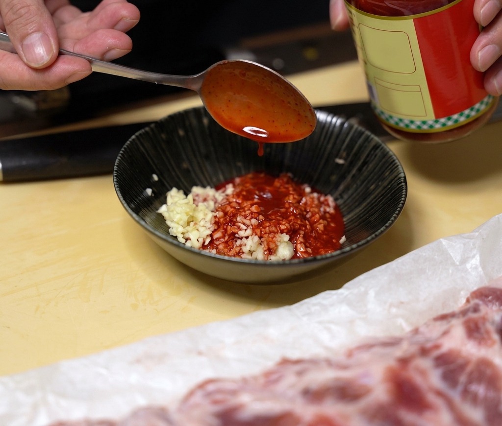 Ein Löffel leuchtend roter fermentierter Tofu-Flüssigkeit wird in eine Schüssel mit gehacktem Knoblauch gegeben.