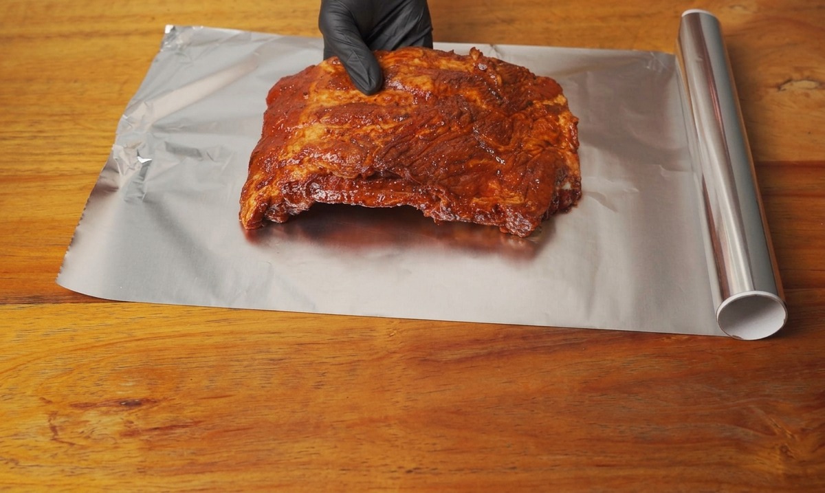 Ein mariniertes Rippchen-Stück wird auf ein großes Blatt Aluminiumfolie gelegt.