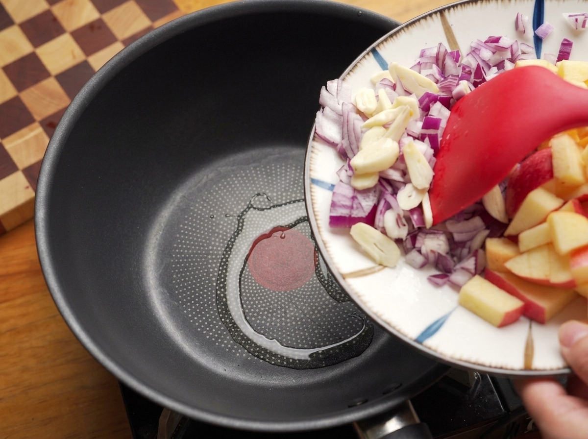 Zwiebeln und Knoblauch werden mit einem Pfannenwender in eine erhitzte Pfanne mit Öl geschoben.
