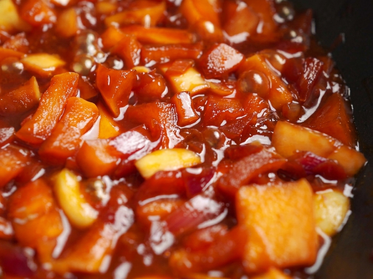 Äpfel und Zwiebeln köcheln in einer sämigen, roten Sauce in der Pfanne.