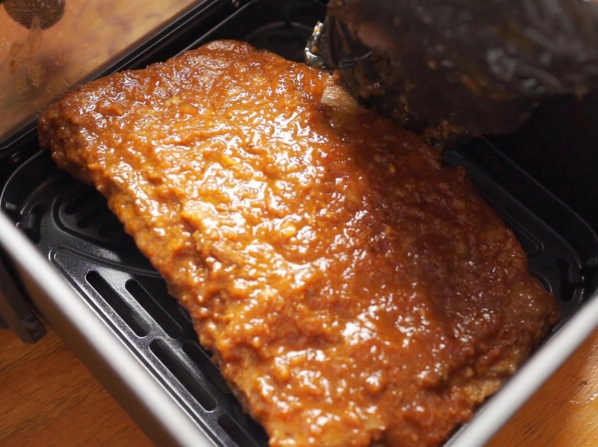 Ein Rippchen-Stück mit glänzender Glasur wird zurück in den Air-Fryer-Korb gelegt.