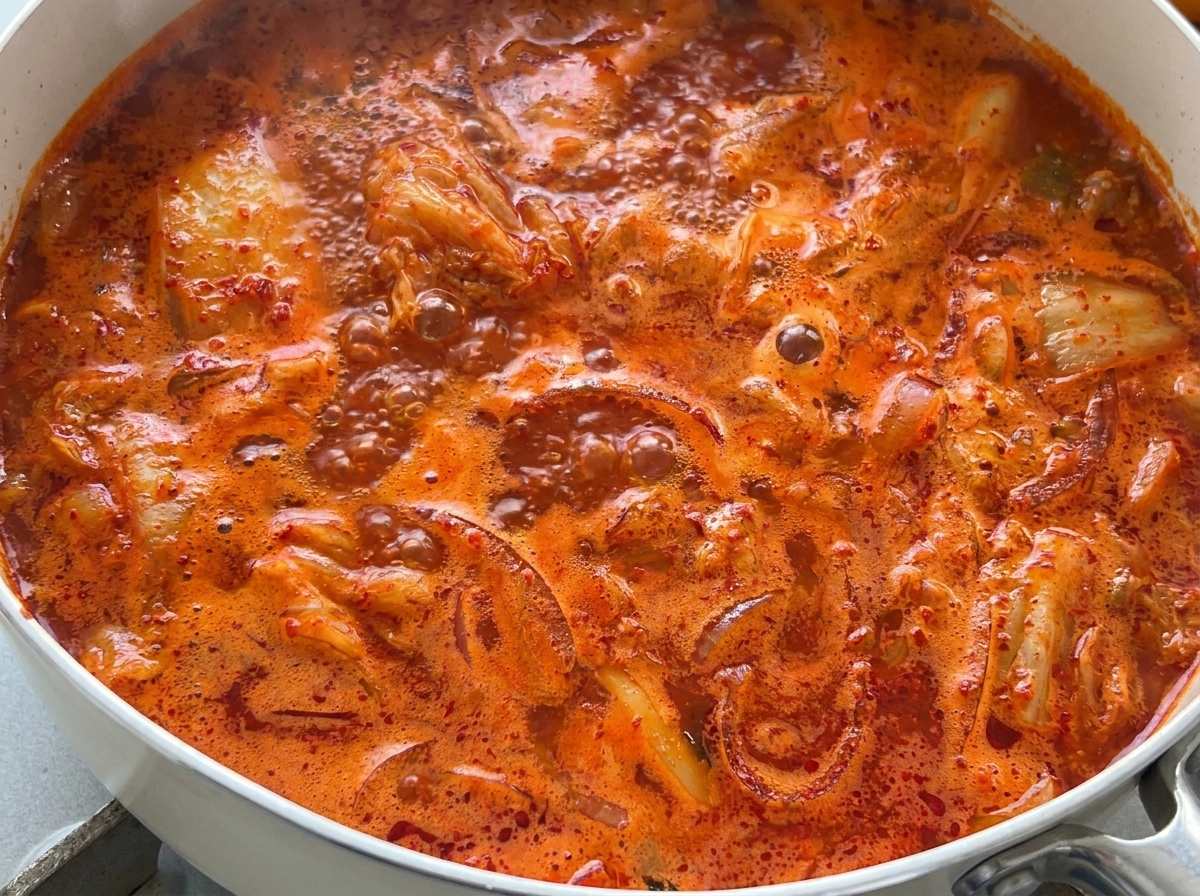 Nahaufnahme einer kräftig kochenden, roten Kimchi-Suppe in einer Pfanne.