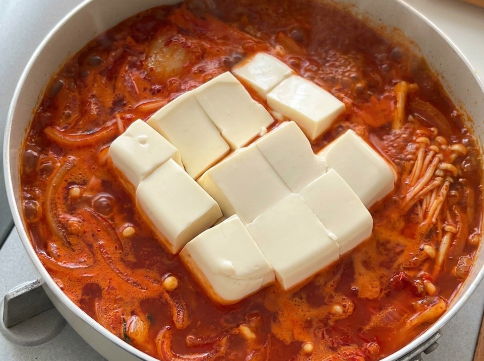 Große Würfel aus weißem Seidentofu in einem sprudelnden koreanischen Kimchi-Eintopf.