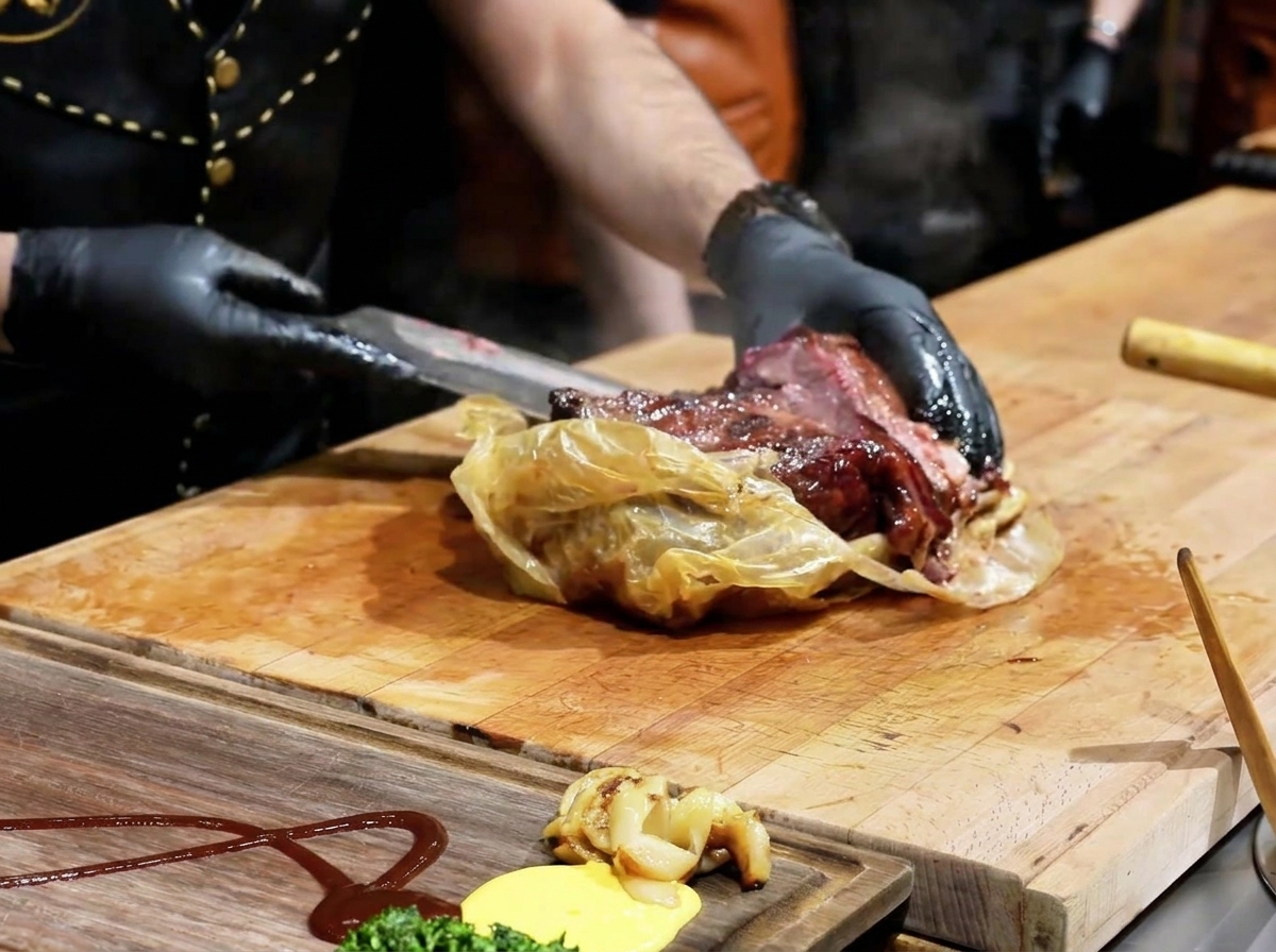 Ein Koch öffnet mit einem Messer die Garhülle und legt ein dunkles, saftiges Brisket auf ein Holzbrett.
