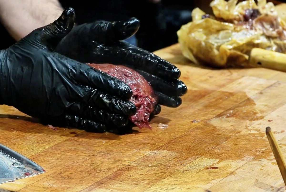 Ein Koch presst mit schwarzen Handschuhen auf ein dunkles Brisket, um das Fleisch zu zerteilen.