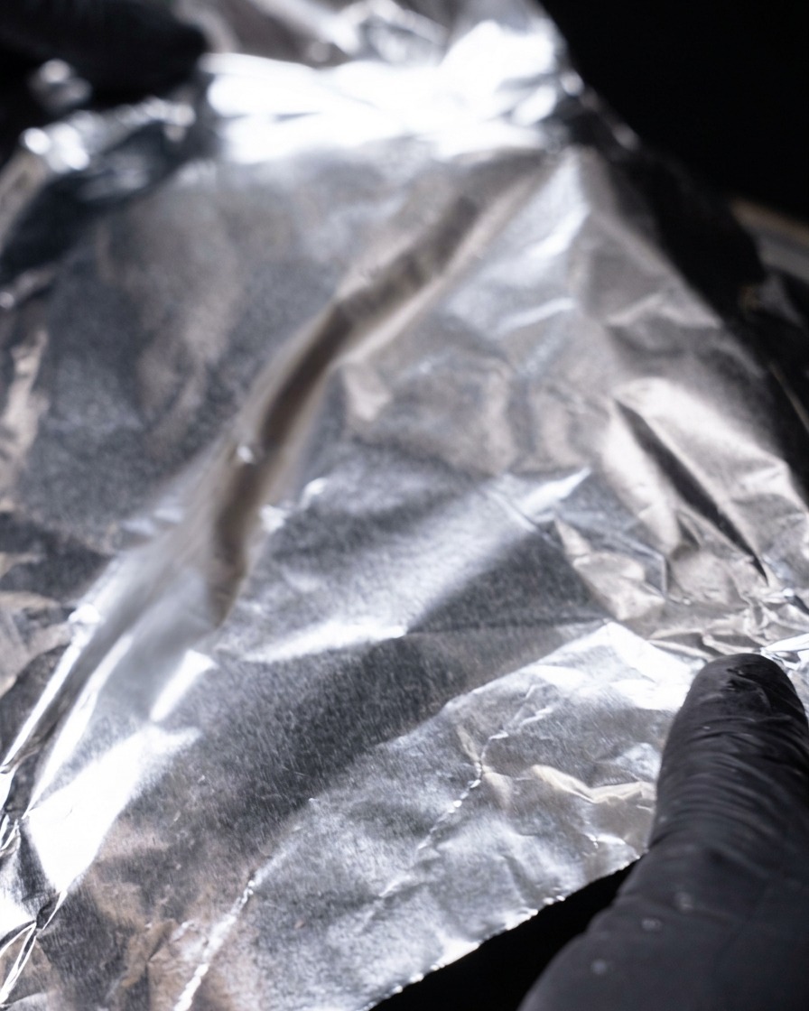 Hände decken die heiße Pfanne komplett mit einer Schicht Aluminiumfolie ab.