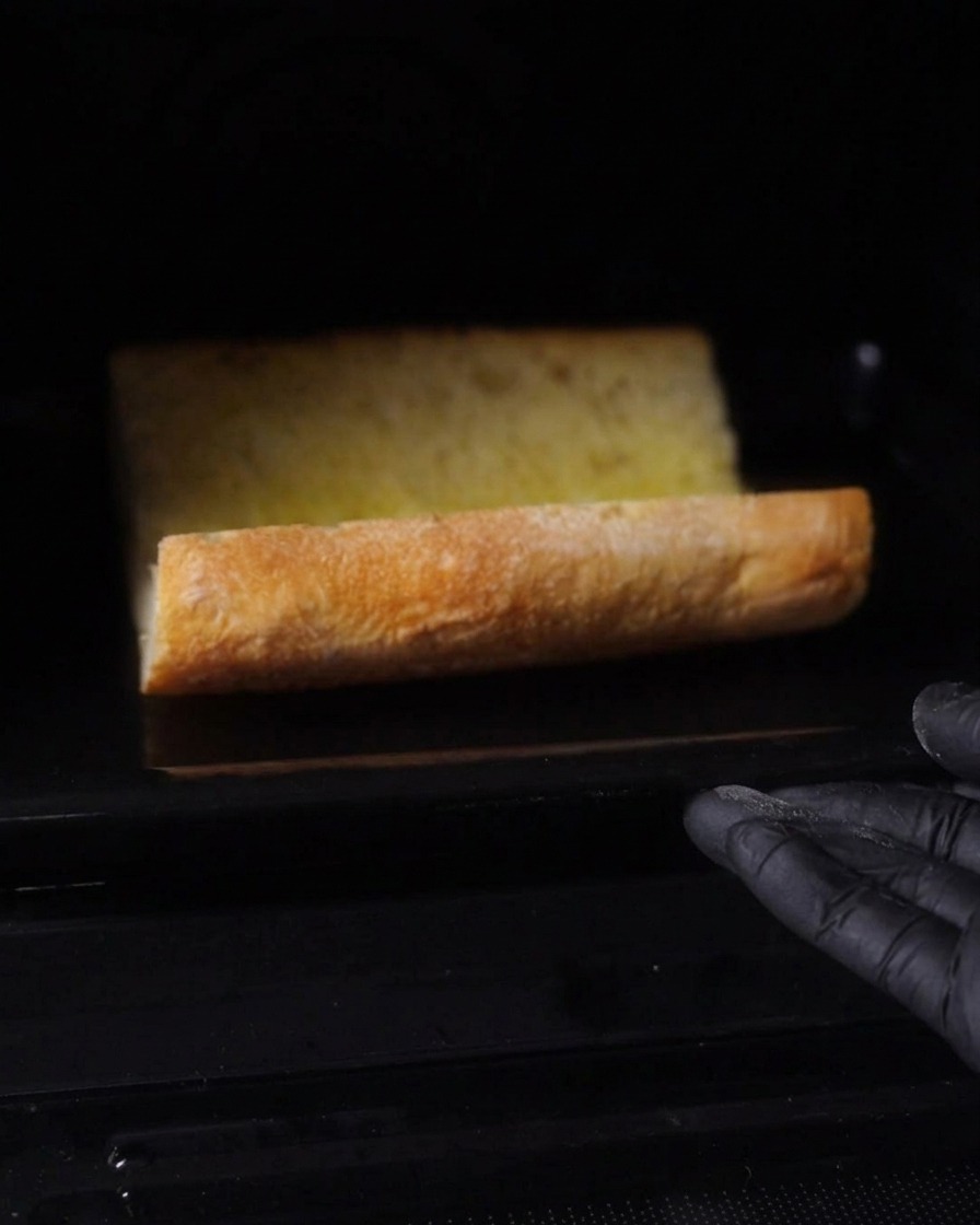 Das gebutterte Baguette wird im dunklen Ofen geröstet.