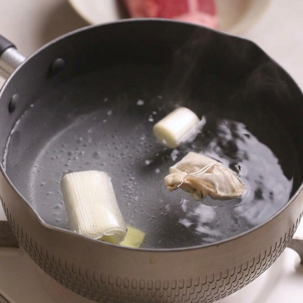 Ein kleiner Topf mit kochendem Wasser, Frühlingszwiebeln, einer Scheibe Ingwer und einem kleinen Gewürzbeutel.