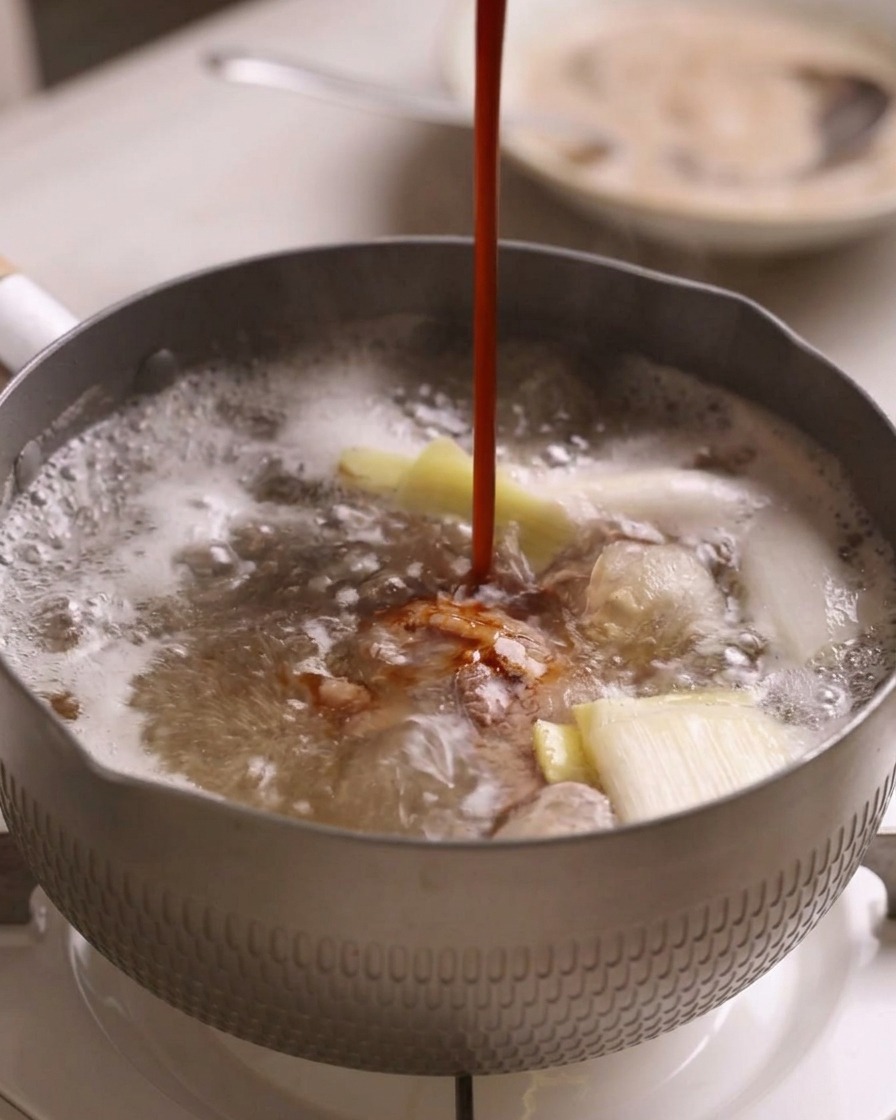 Eine dunkelrote Schmorsauce wird in den Topf mit dem kochenden Fleisch und den Aromaten gegossen.