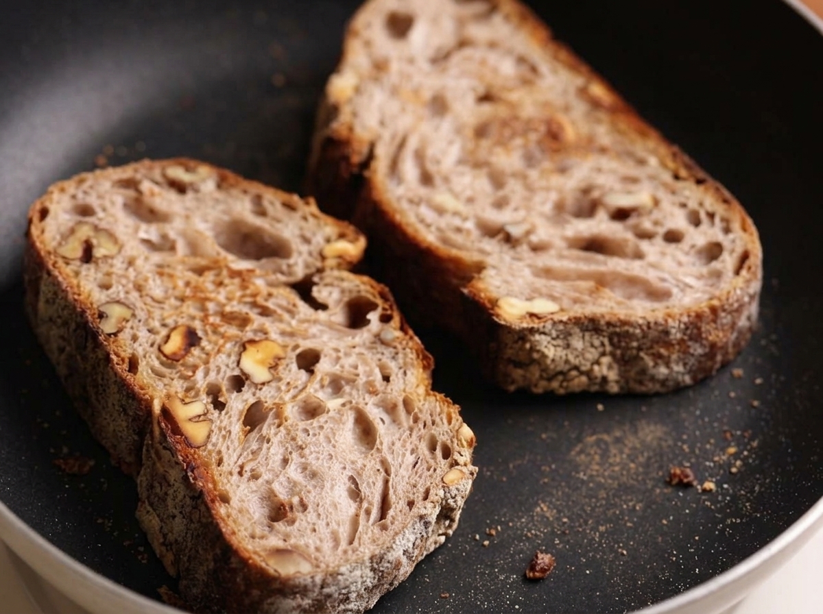 Zwei Scheiben rustikales Bauernbrot werden in einer flachen Pfanne ohne Fett geröstet.