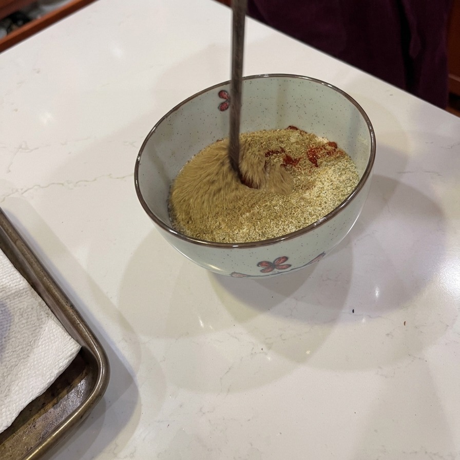 Ein Holzutensil rührt Mehl und rötlich-braune Gewürze in einer Schüssel zusammen.