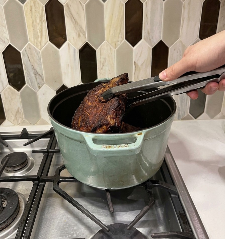 Scharf angebratene Fleischstücke werden mit einer Metallzange in einen hellgrünen Dutch Oven gelegt.