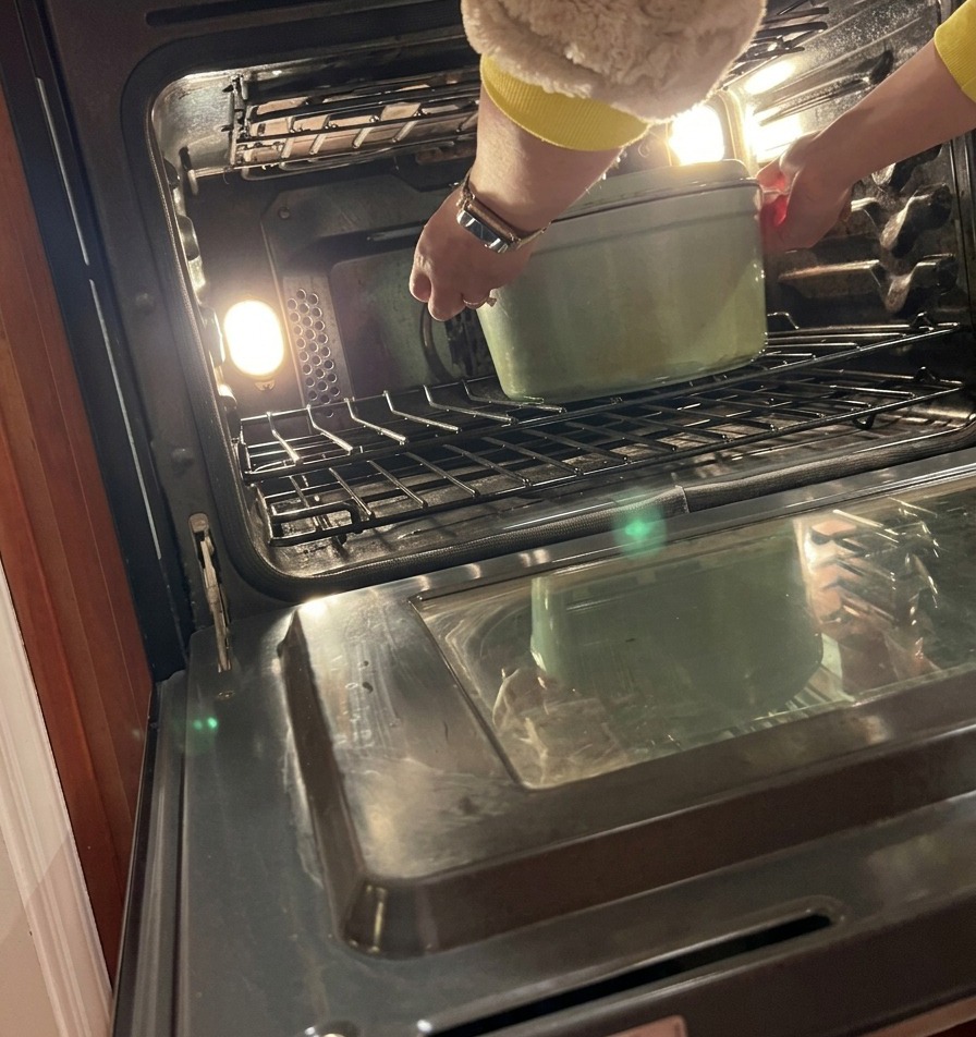 Eine Person stellt einen geschlossenen Dutch Oven auf die mittlere Schiene eines vorgeheizten Backofens.