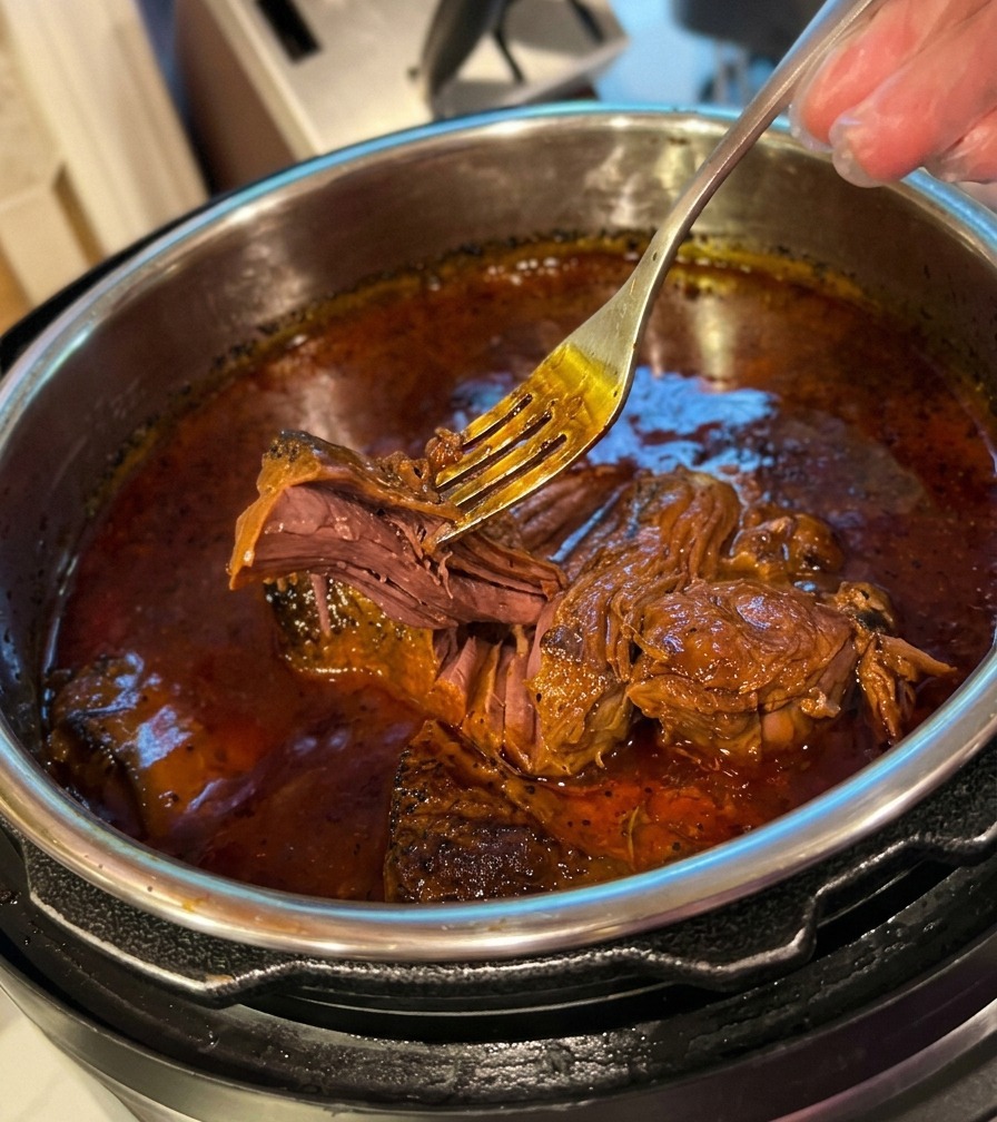 Eine Gabel zerteilt mühelos extrem zartes, geschmortes Rindfleisch in einer dunklen Sauce im Topf.
