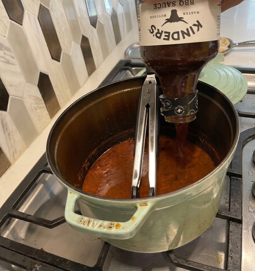 Eine Flasche BBQ-Sauce wird in den Topf mit der reduzierten Schmorflüssigkeit gegossen.