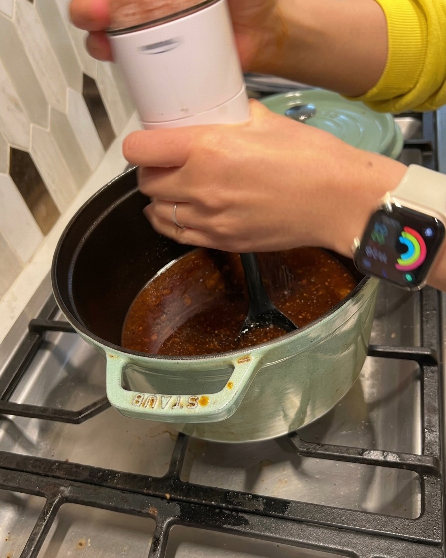 Salz und schwarzer Pfeffer werden aus einer Mühle in die simmernde dunkle Sauce im Topf gemahlen.