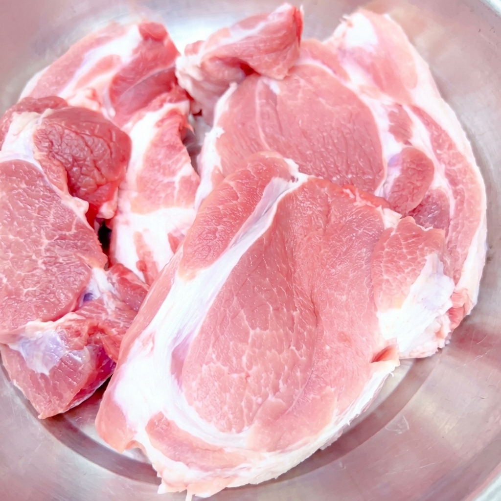 Große Stücke rohes Schweinefleisch in einer Edelstahlschüssel.