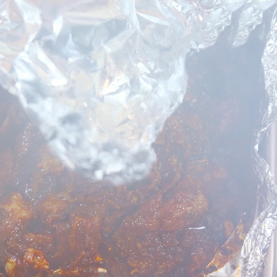 Dampf steigt aus einem geöffneten Folienpaket auf und gibt den Blick auf dunkles, gegartes Fleisch frei.