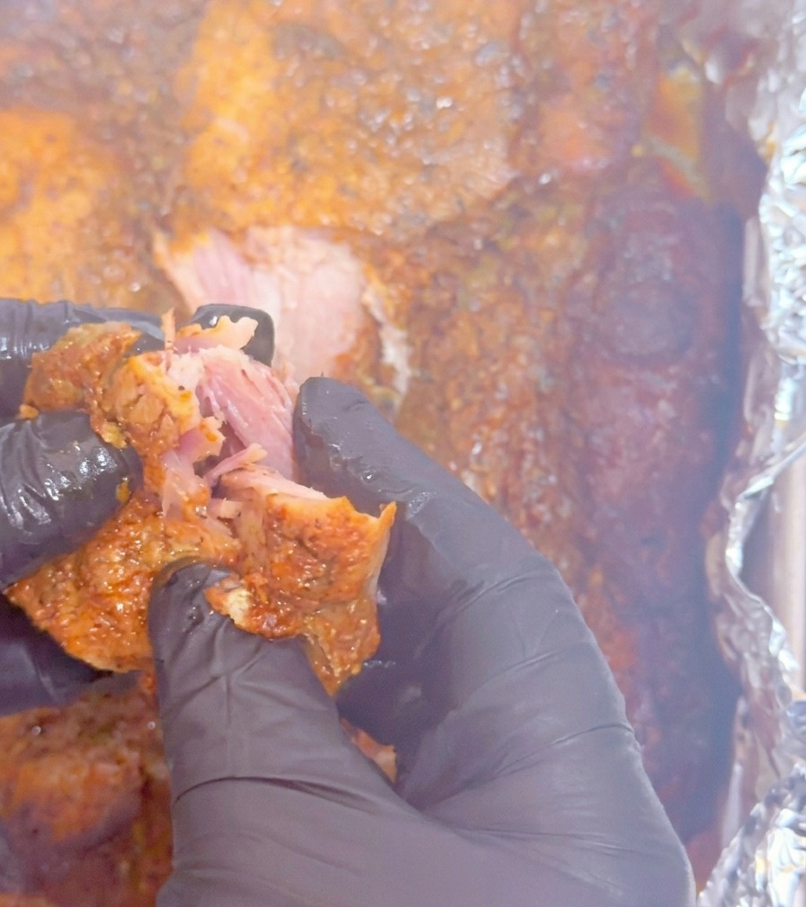 Hände zupfen ein zartes Stück Fleisch in feine, saftige Fasern auseinander.