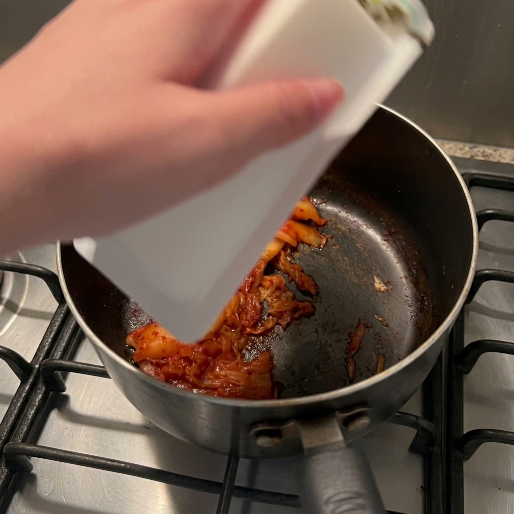 Ein Block weißer Seidentofu gleitet aus der Packung in den Topf zum angebratenen Kimchi.