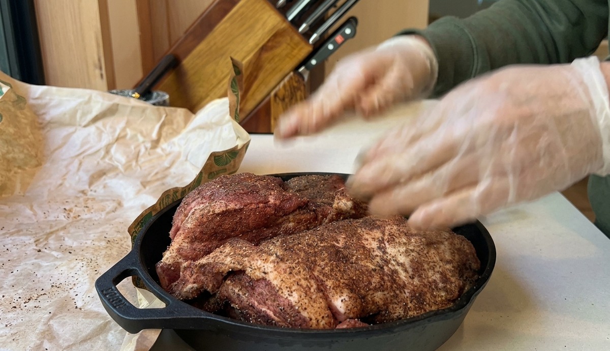 Eine gewürzte Schweineschulter liegt in einer gusseisernen Pfanne bereit für den Backofen.