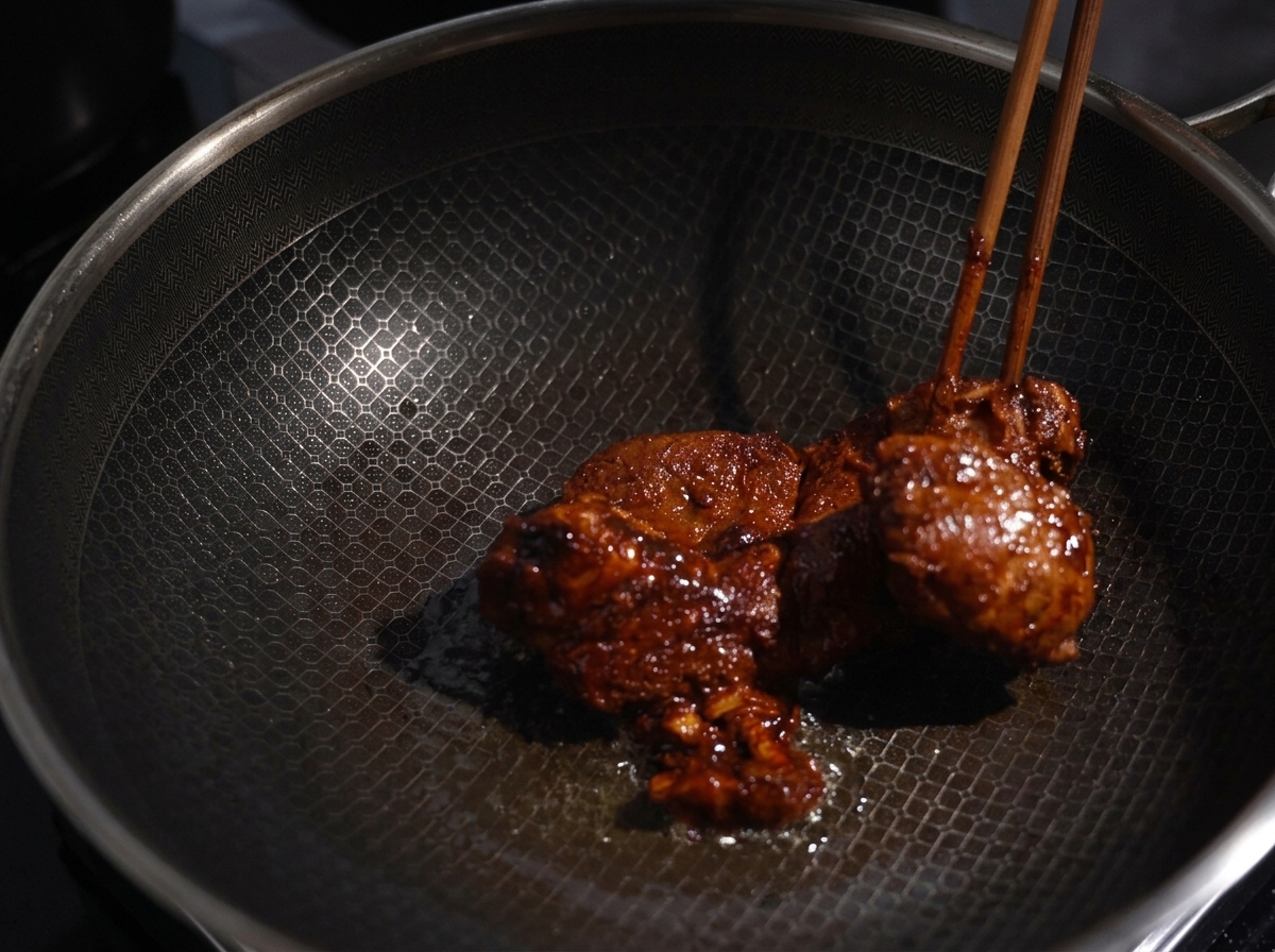 Marinierte Schweinefleischstücke werden in einem heißen Wok angebraten, bis eine dunkle Kruste entsteht.