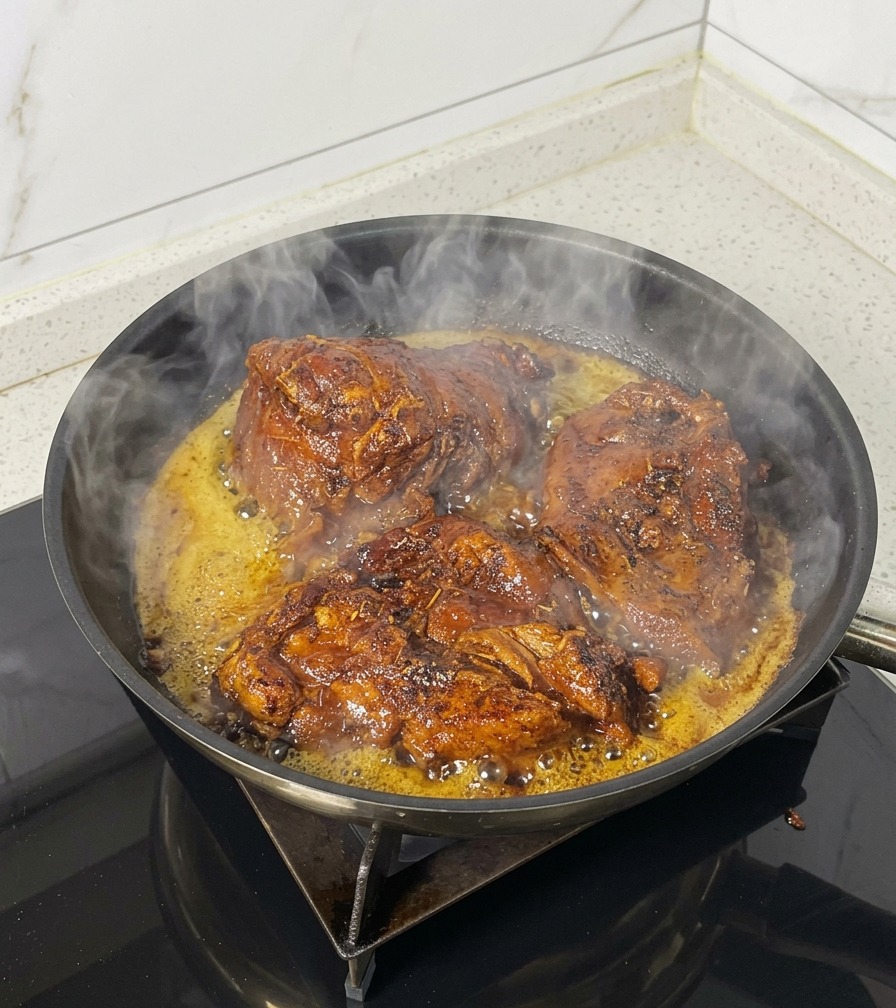 Drei große Stücke Fleisch brutzeln in einer schwarzen Pfanne mit dampfendem Öl.