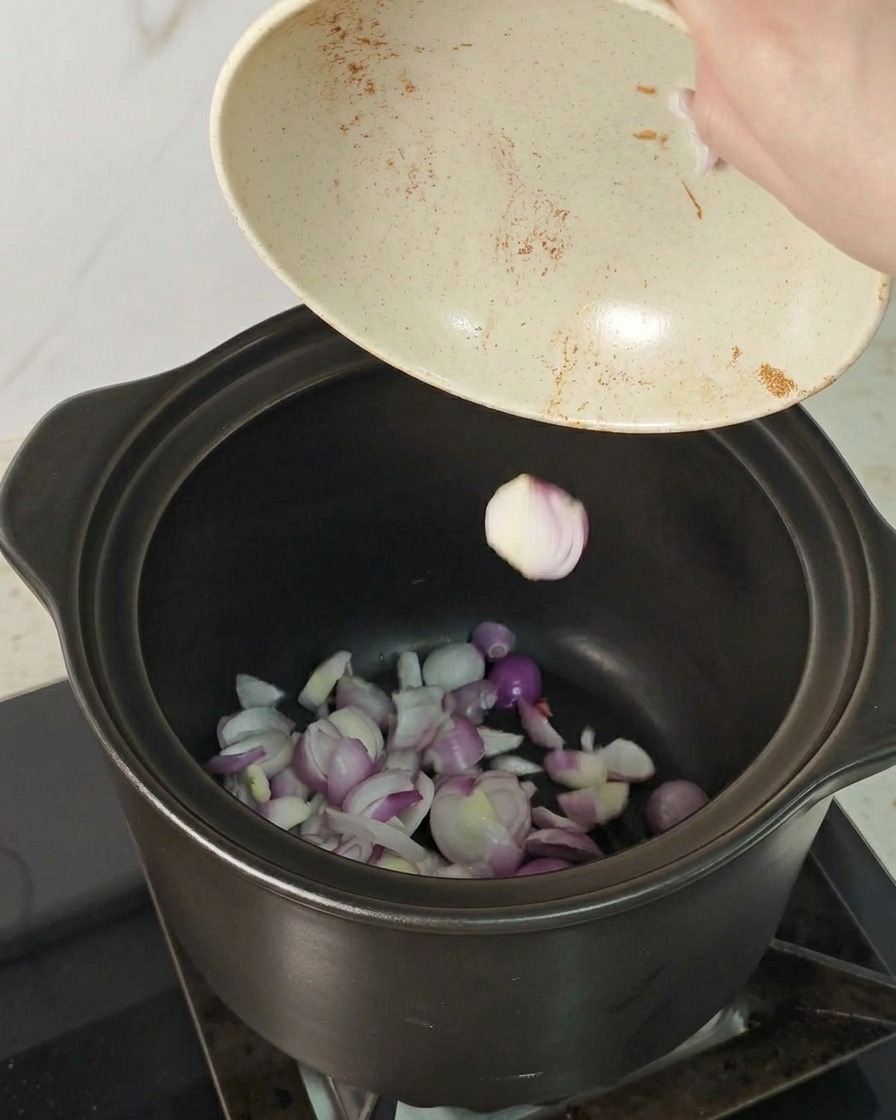 Rote Schalottenscheiben werden in den Boden eines dunklen Keramiktopfes geschüttet.
