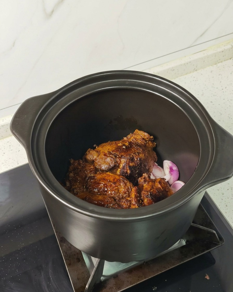 Scharf angebratene Fleischstücke ruhen auf Schalottenscheiben in einem dunklen Schmortopf.