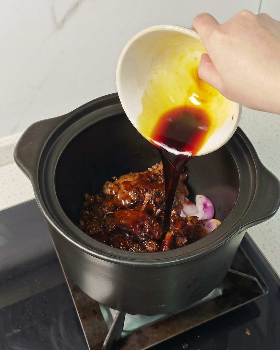 Eine Hand gießt eine dunkle Sauce aus einer kleinen Schüssel über das Fleisch im Topf.