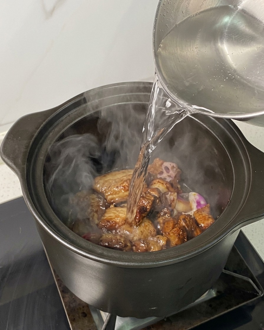 Heißes Wasser wird aus einem Kessel über das Fleisch und die Zwiebeln im Topf gegossen.