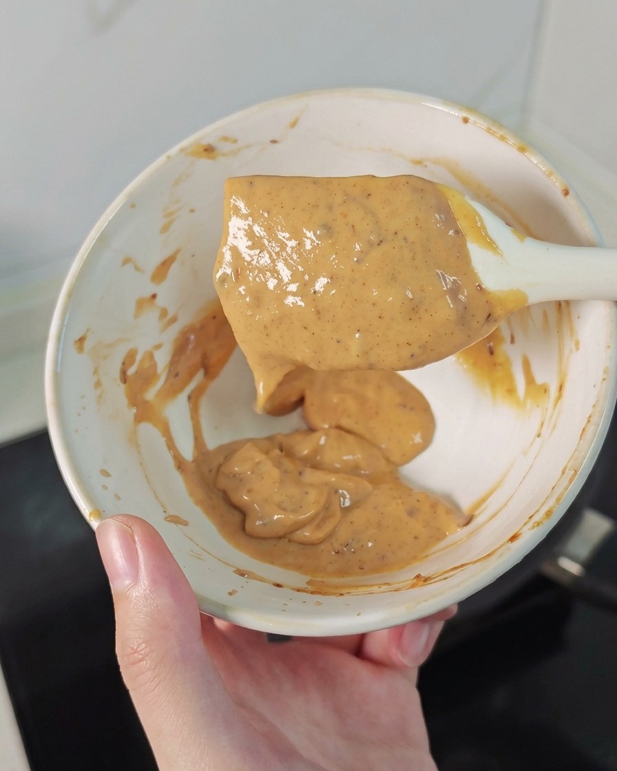 Eine Hand hält eine Schüssel mit einer cremigen, leicht orangefarbenen Sauce.