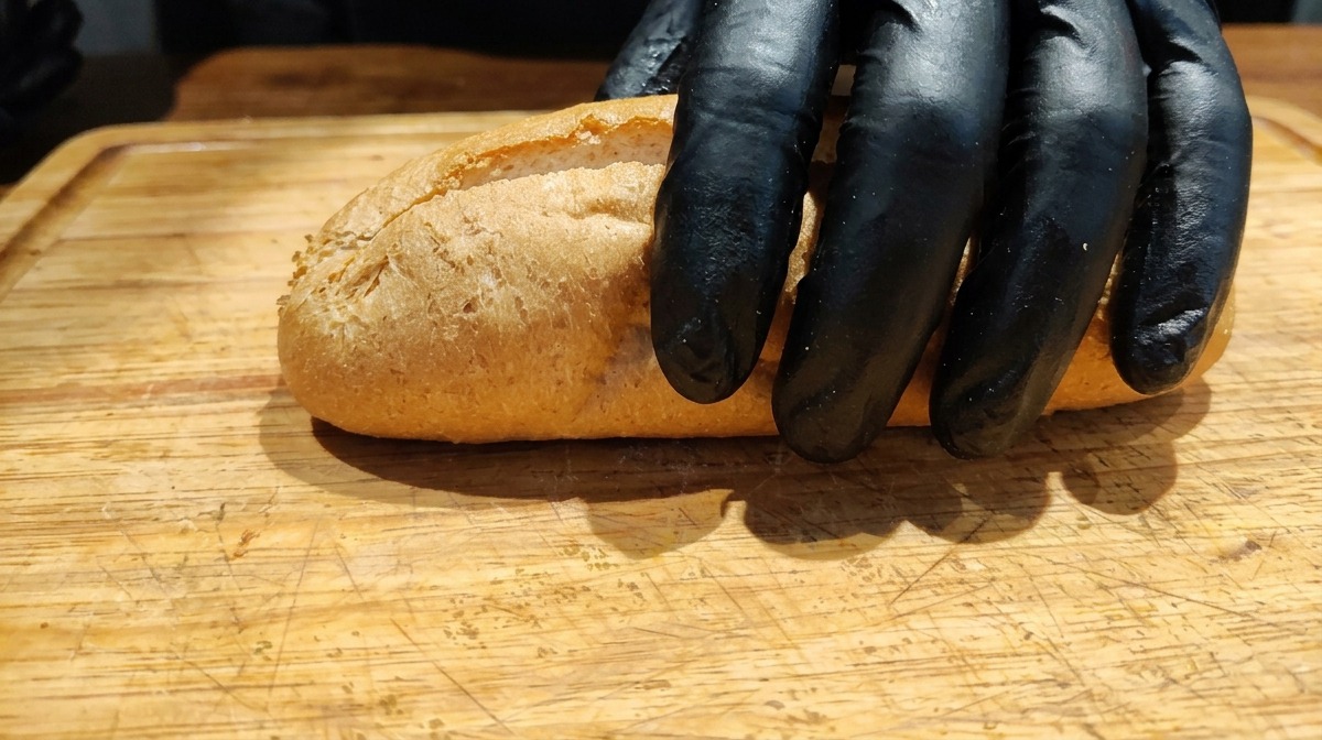 Eine Hand platziert ein aufgeschnittenes Vollkornbaguette auf einem Holzbrett.