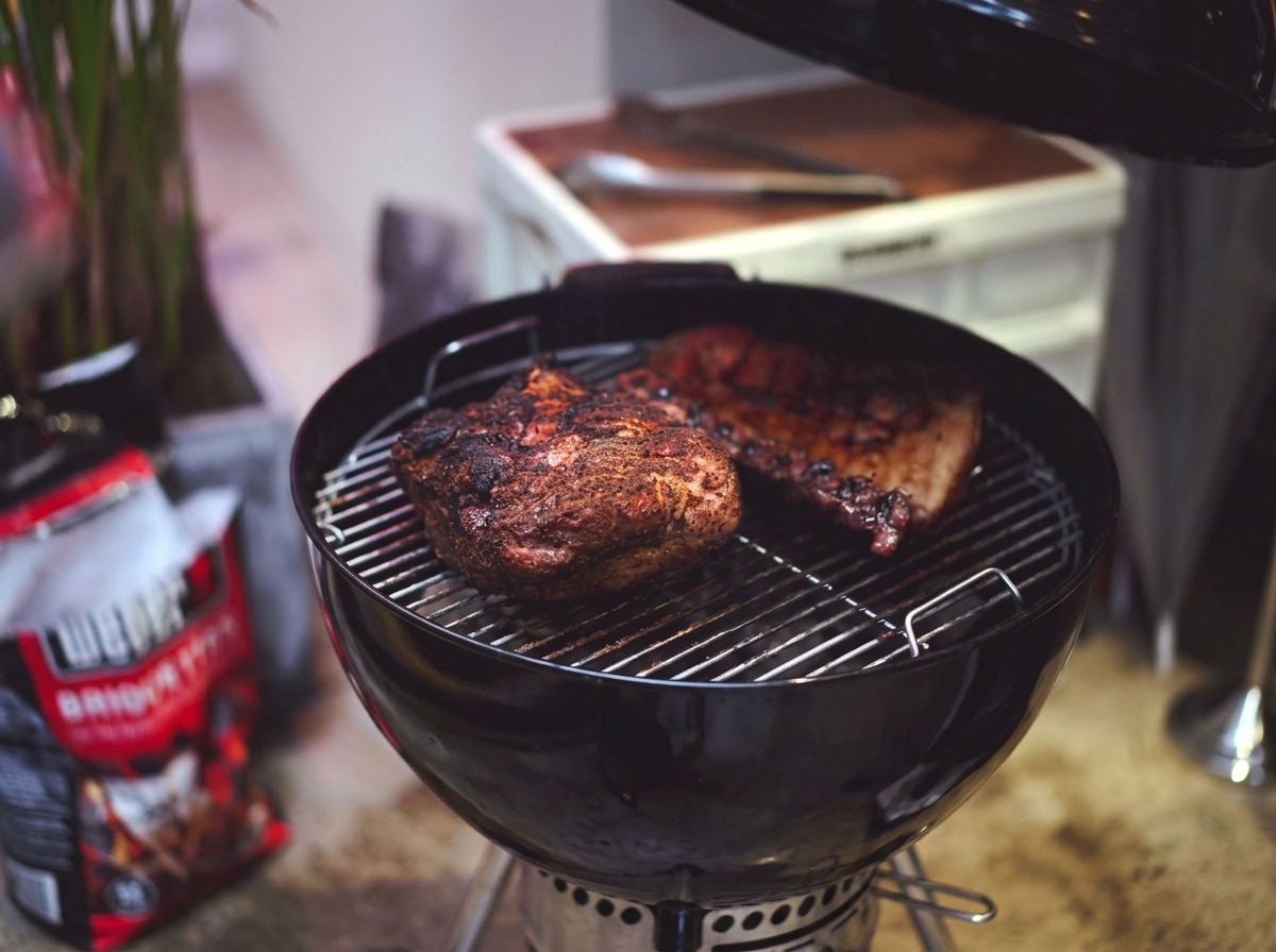 Teilweise gegarte Schweineschulter und Rippchen mit einer dunklen, karamellisierten Kruste auf dem Grillrost.