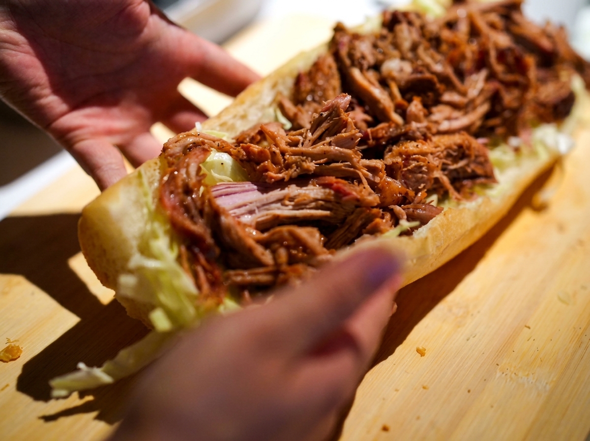 Hände halten ein Sandwich-Brötchen, das reichlich mit Coleslaw und saftigem Pulled Pork gefüllt ist.