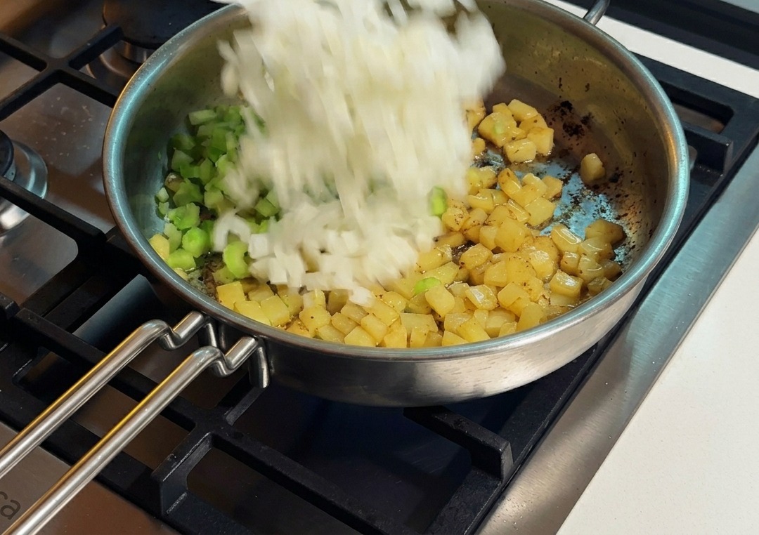 Zwiebeln und Sellerie werden zu den Kartoffeln in die Edelstahlpfanne gegeben.