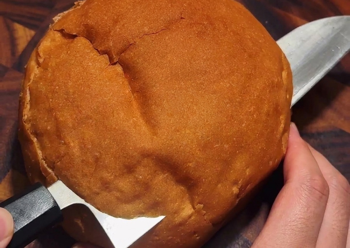 Ein Messer schneidet einen Deckel in die Oberseite eines runden Brotlaibs.
